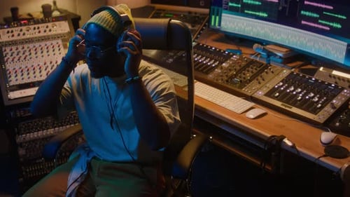 Black Male Record Producer Listening to Track and Adjusting Output in Studio