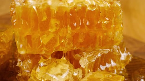 Streams of golden honey drip and pour onto the honeycomb lying on a wooden oak cutting boad