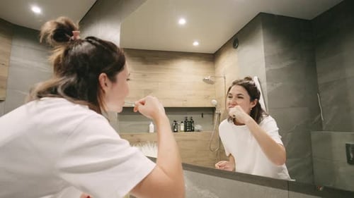 Una joven se cepilla los dientes frente al espejo del baño cuidando su higiene bucal