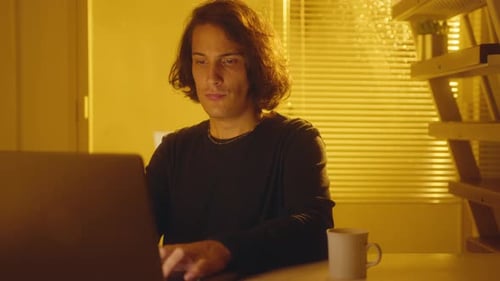 Young Man Working on Laptop in Office with Yellow Light