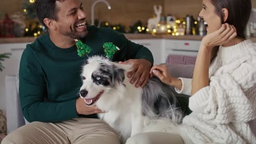 Couple Petting Dog Wearing Christmas Antlers at Home