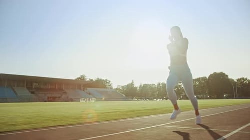 Beautiful Fitness Woman in Light Blue Athletic Top and Leggings Jogging in a Stadium. She is Runnin