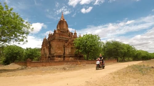Une fille fait de la moto sur une route tranquille devant un grand temple.