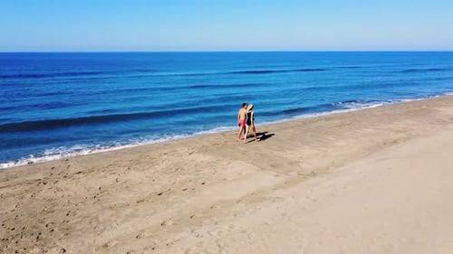Drone view of couple, man, woman walking together along shore of beach of sea