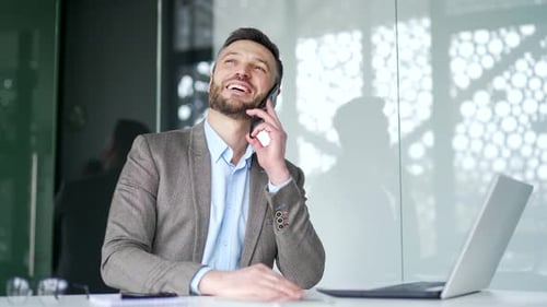 Happy businessman talking on phone while sitting at workplace in business office. Smiling handsome