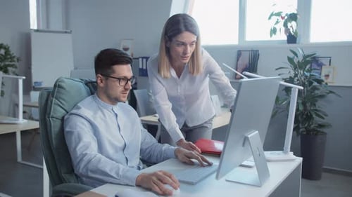 Attractive Man and Woman Talking Use Computer Working Together in a Modern Office On Background