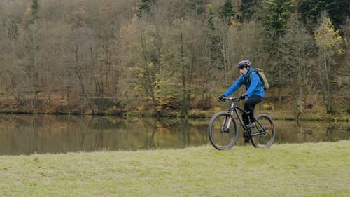 Young man cycling through autumn forest landscape near beautiful lake
