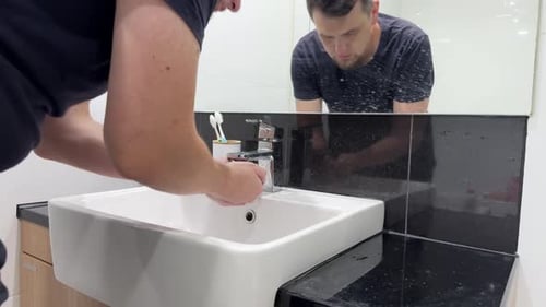 Un hombre se lava la cara en el lavabo del baño mientras se prepara para el día