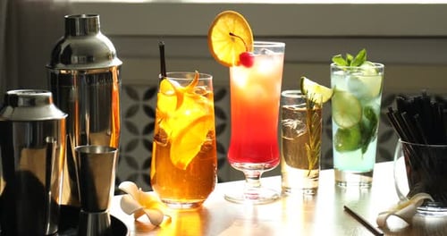 Des verres de différents délicieux cocktails rafraîchissants, des shakers, un doseur et des pailles sur la table.