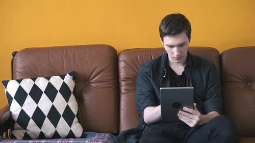 Young Man Using Tablet on Couch Indoors