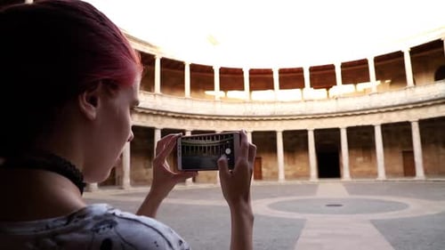 Redhead girl making a photograph with smartphone to a monument in slow motion, Granada, Spain