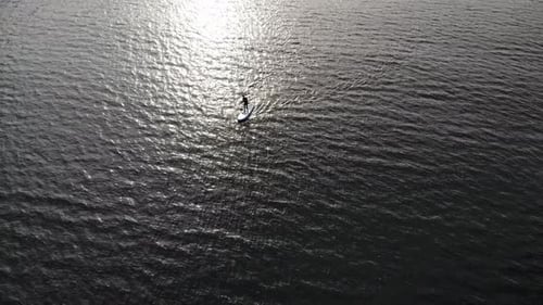 Drone footage of a backlit person on stand up paddle-board on water
