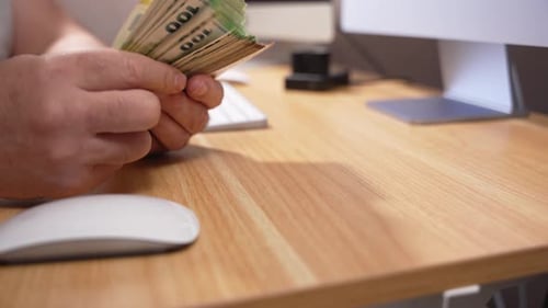Man Counting Stack of Money at Wooden Desk