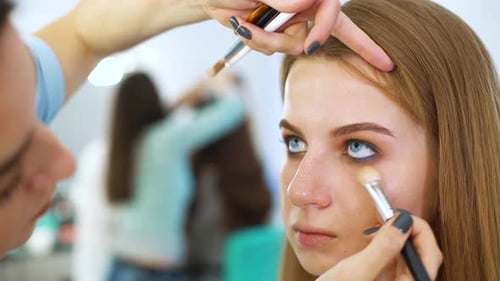 Female makeup artist doing professional makeup for young red hair woman at beauty salon