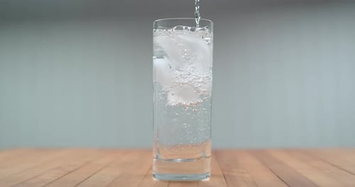 Clear sparkling water being poured into glass with ice