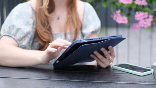 A Girl Works on a Tablet While Sitting at a Table in a Summer Cafe