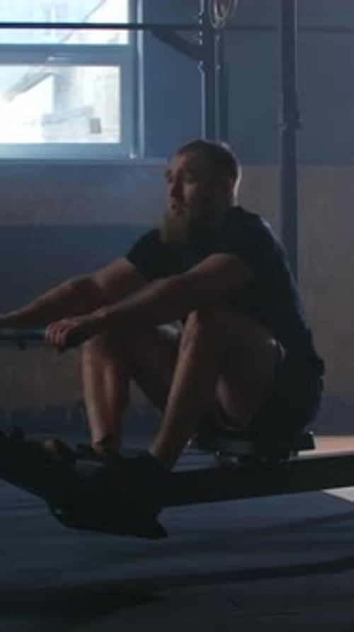 Man Rows on Rowing Machine in Gym