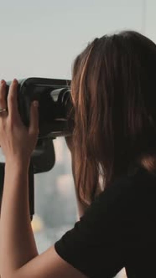 Woman Looks Through Binoculars on a Building