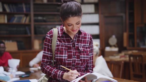 Concentrated young woman writes in notebook while studying in a university library