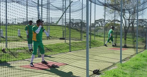Senior coach tossing baseball at mid adult man practicing swing in batting cage, copy space