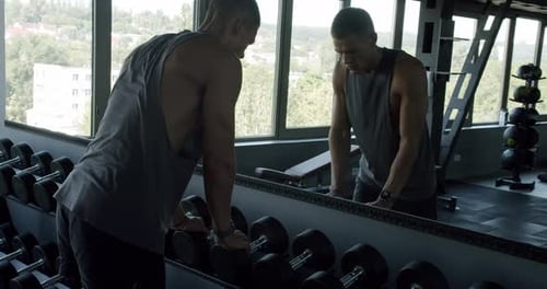 Junger Mann wählt Hanteln in einem modernen Fitnessstudio aus — Fitnessziele
