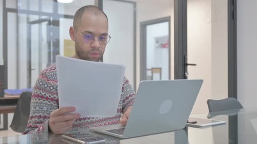 Young Adult Working on Laptop Reviewing Documents