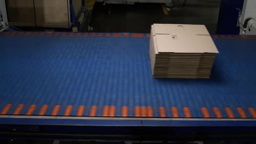 La cinta transportadora azul transporta una pila de cajas de cartón dobladas
