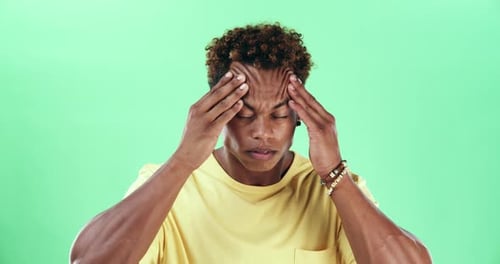 A young man suffering from a headache against a green studio background