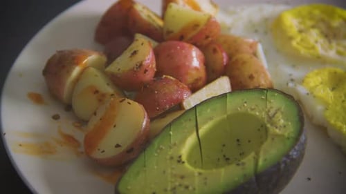 person eating a healthy breakfast of avocado, potatoes and eggs