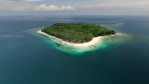 Flying to a paradise island in the ocean, tilting down on boats and white sand beach.