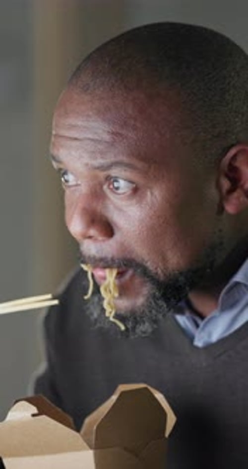 Black man in office at night, eating fast food at computer and reading email