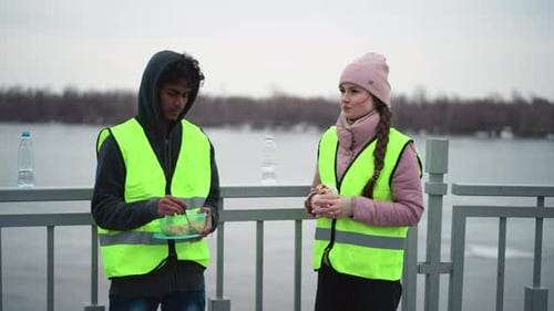 Man in Hoodie and Neon Safety Vest Eating From Container Outdoor Work