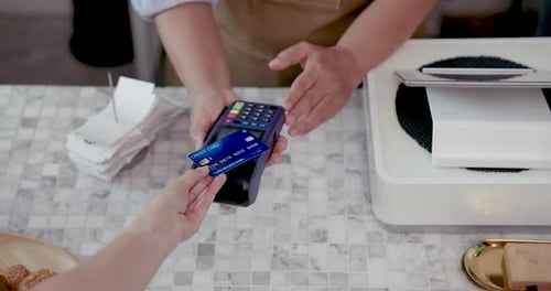 Hands holding credit card near payment terminal during transaction with asian senior cashier at