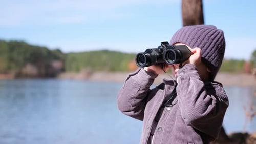 Curious Boy Exploring Nature Using Binoculars By a Lake