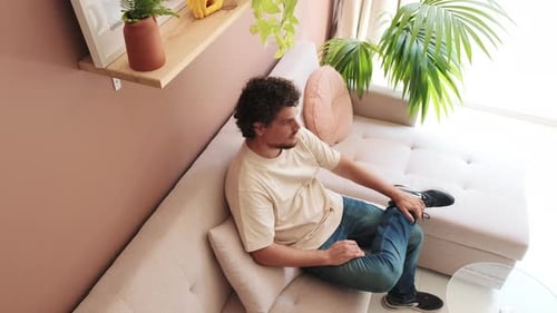 Guy relaxing sitting on the sofa in cozy living room, view from above