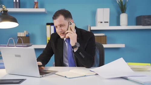 Smiling Man Talking on Phone While Using Laptop
