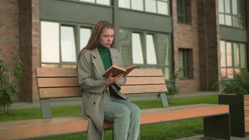 Woman Reading Book on Bench in Urban Setting