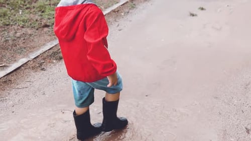 Kid walking in slow motion in a muddy puddle at the park. Enjoying outdoors on a rainy day. Child go