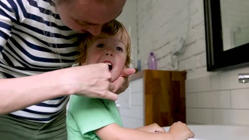 Woman Brushing Child's Teeth in Bathroom