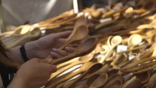 woman feels wooden spoons at a craft market, can't decide