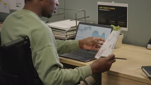 Schwarzer männlicher Büroangestellter im Rollstuhl analysiert Geschäftsdiagramme