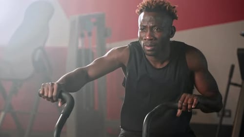 Athletic African American Man is Spinning Pedals of Exercise Bike in Gym Hard Cardio Training