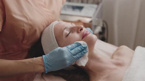 Professional Cosmetologist Cleansing Woman's Face in Spa