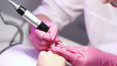 Close-up of a girl doing a manicure in a beauty salon. Nail care. Manicurist in pink gloves removes