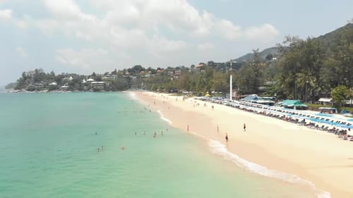 Tropical Andaman sea touching the Karon Beach soft sand crowded with tourists, in Phuket, Thailand -