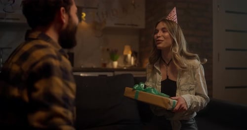 Happy Birthday Girl in a Festive Cap Receives a Gift Box with a Bow From Her Boyfriend During a