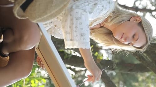 A Blonde Girl Paints on a Canvas Outdoors in the Summer Standing Under the Sun in the Park