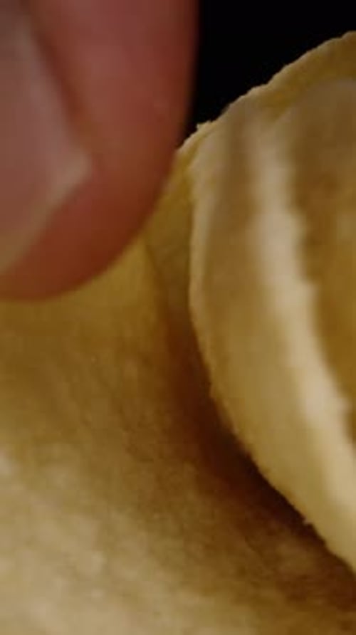 Vertical video. Saddle-shaped corn chips scattered on the table, and I pick them up one by one while