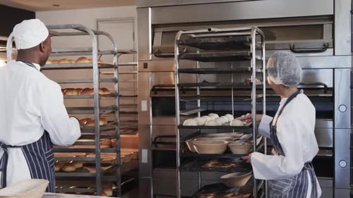 Happy diverse bakers in bakery kitchen preparing rolls in slow motion