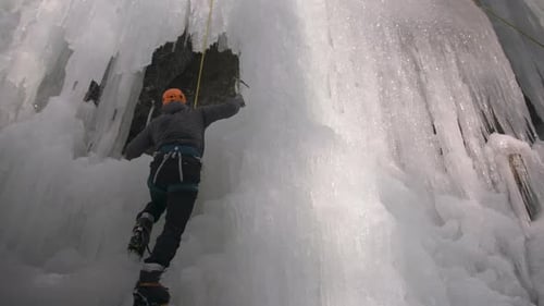 Blick aus der Vogelperspektive auf einen Eiskletterer, der eine riesige Eiswand bewältigt
